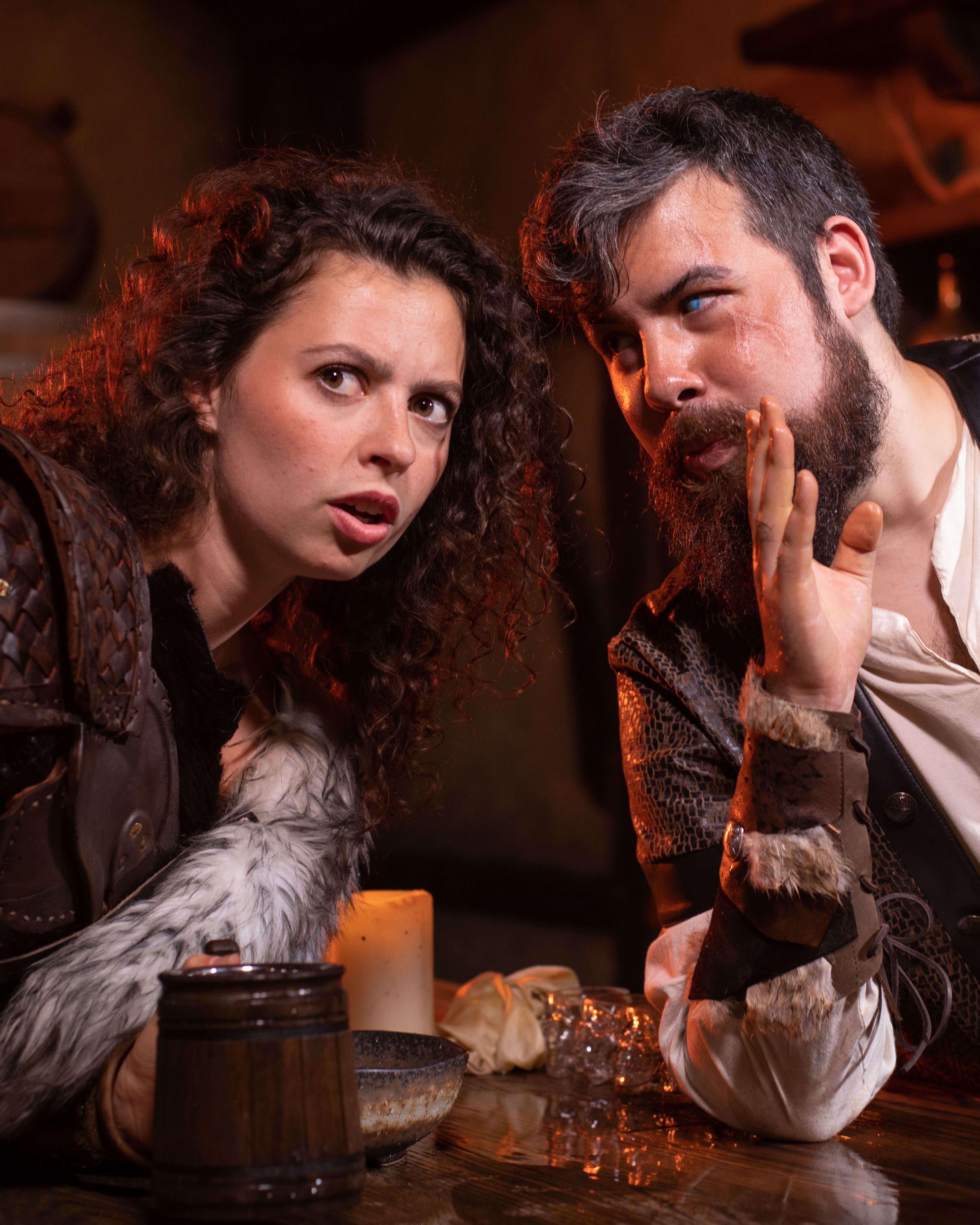 A man and woman in a tavern set in a Dungeons and Dragons story whisper to one another